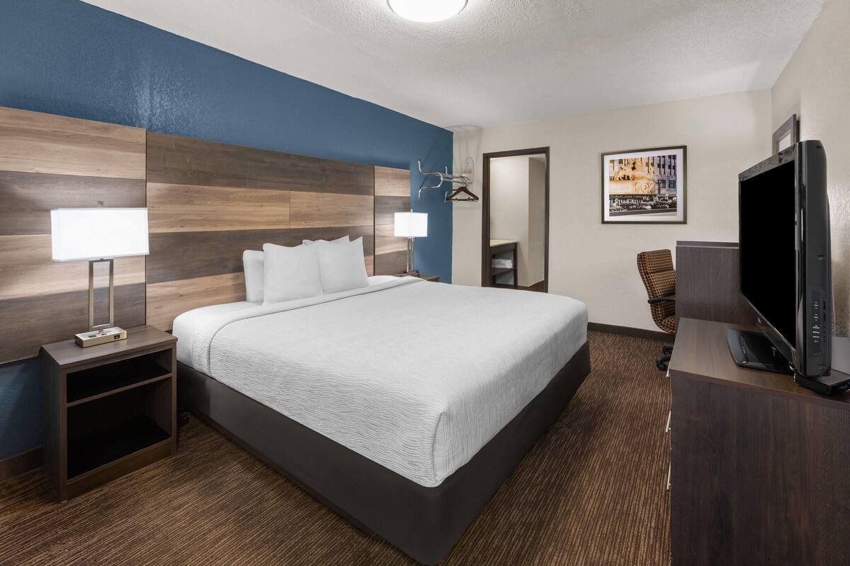 A hotel room with a large bed, a flat-screen TV, a nightstand, and a wall-mounted TV.