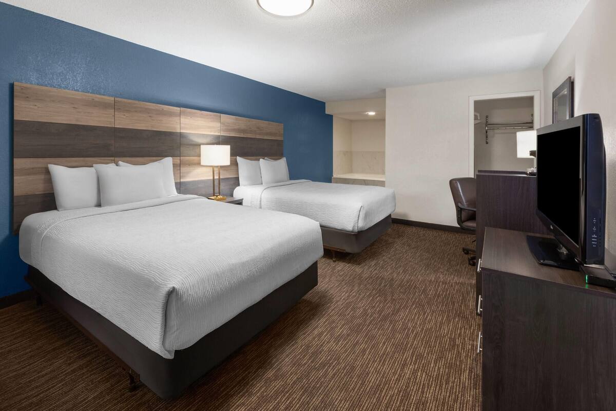 A hotel room with two beds, a desk with a computer, a TV, and a bathroom visible through an open door.