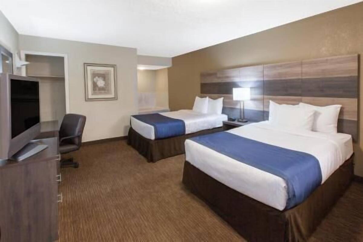 A hotel room with two beds, a desk, a chair, a TV, and a framed picture on the wall.
