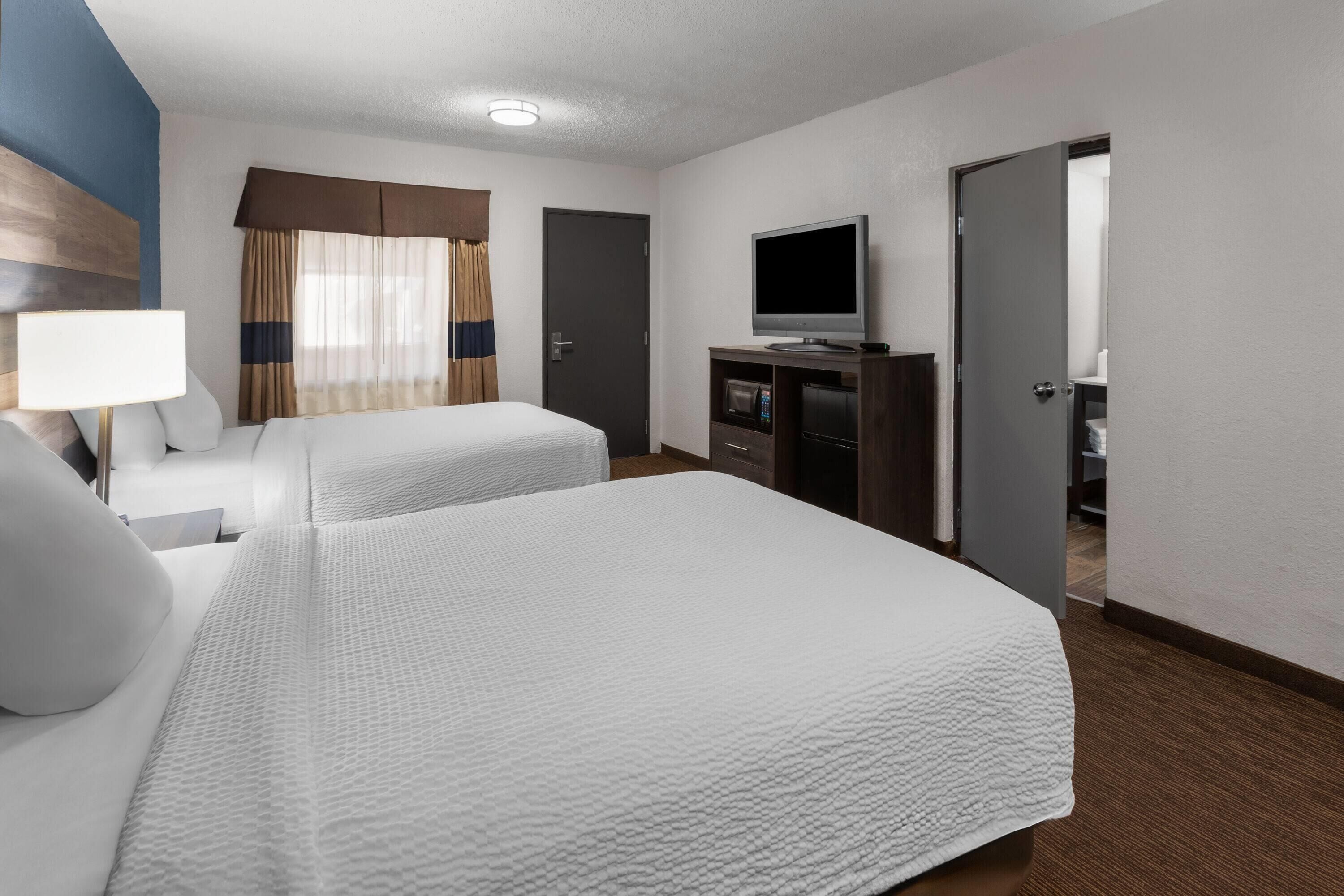 Una habitación de hotel con dos camas, televisión, escritorio con computadora y puerta que da a otra habitación.