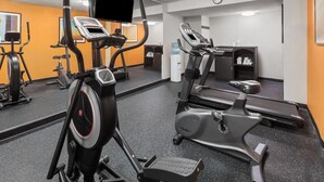 Une salle de sport équipée d’appareils de cardio, de miroirs et d’une horloge au mur.