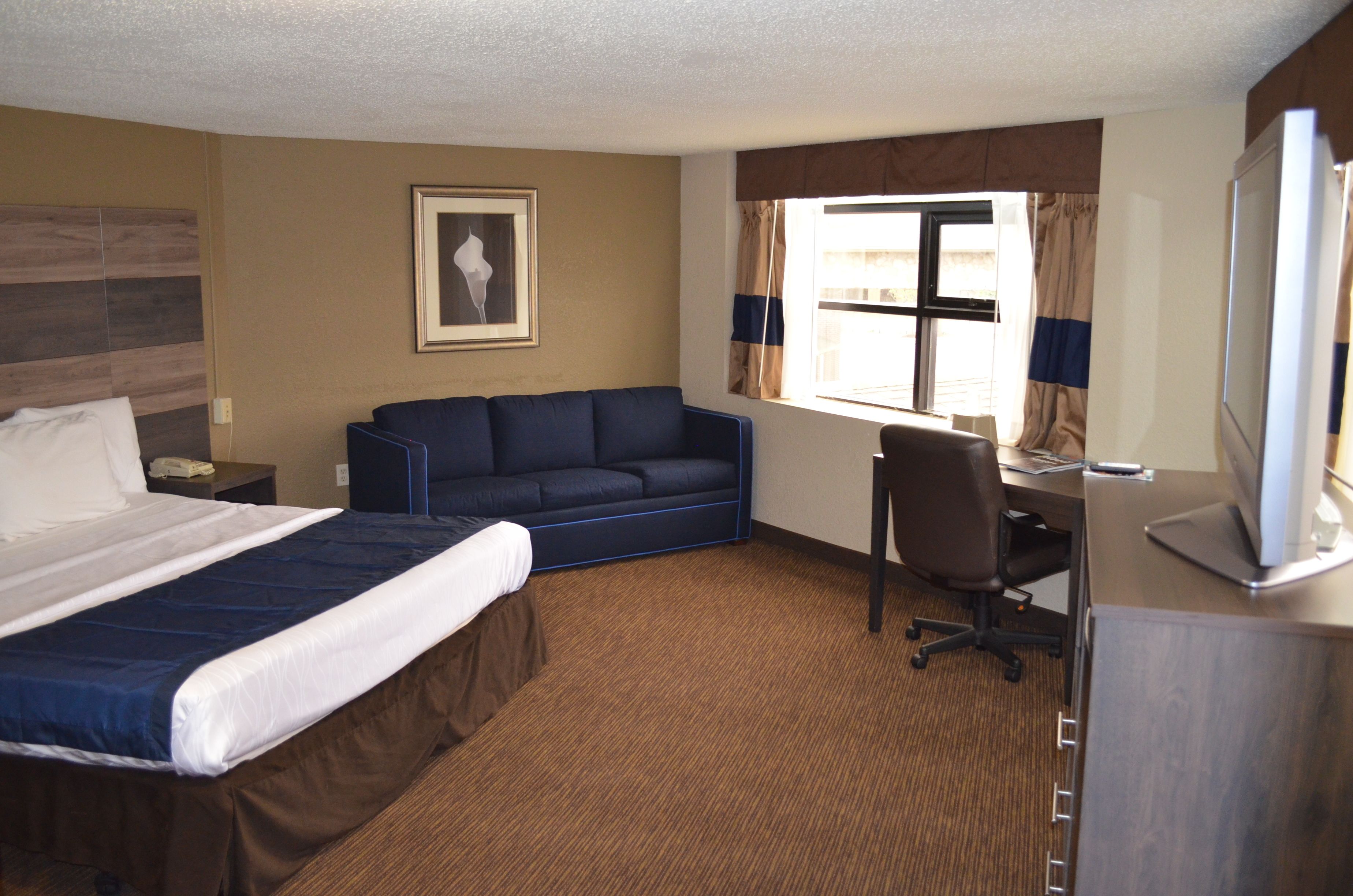 A hotel room with a large bed, a sofa, a desk, and a TV.