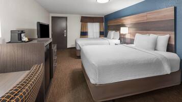 A hotel room with two beds, a desk with a coffee maker, a TV, and a lamp.