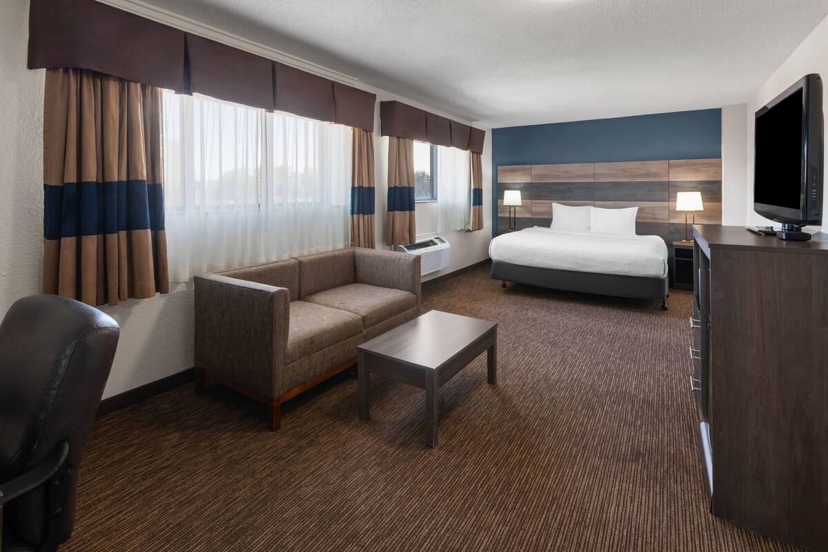 A hotel room with a bed, a sofa, a coffee table, a TV, and a desk.