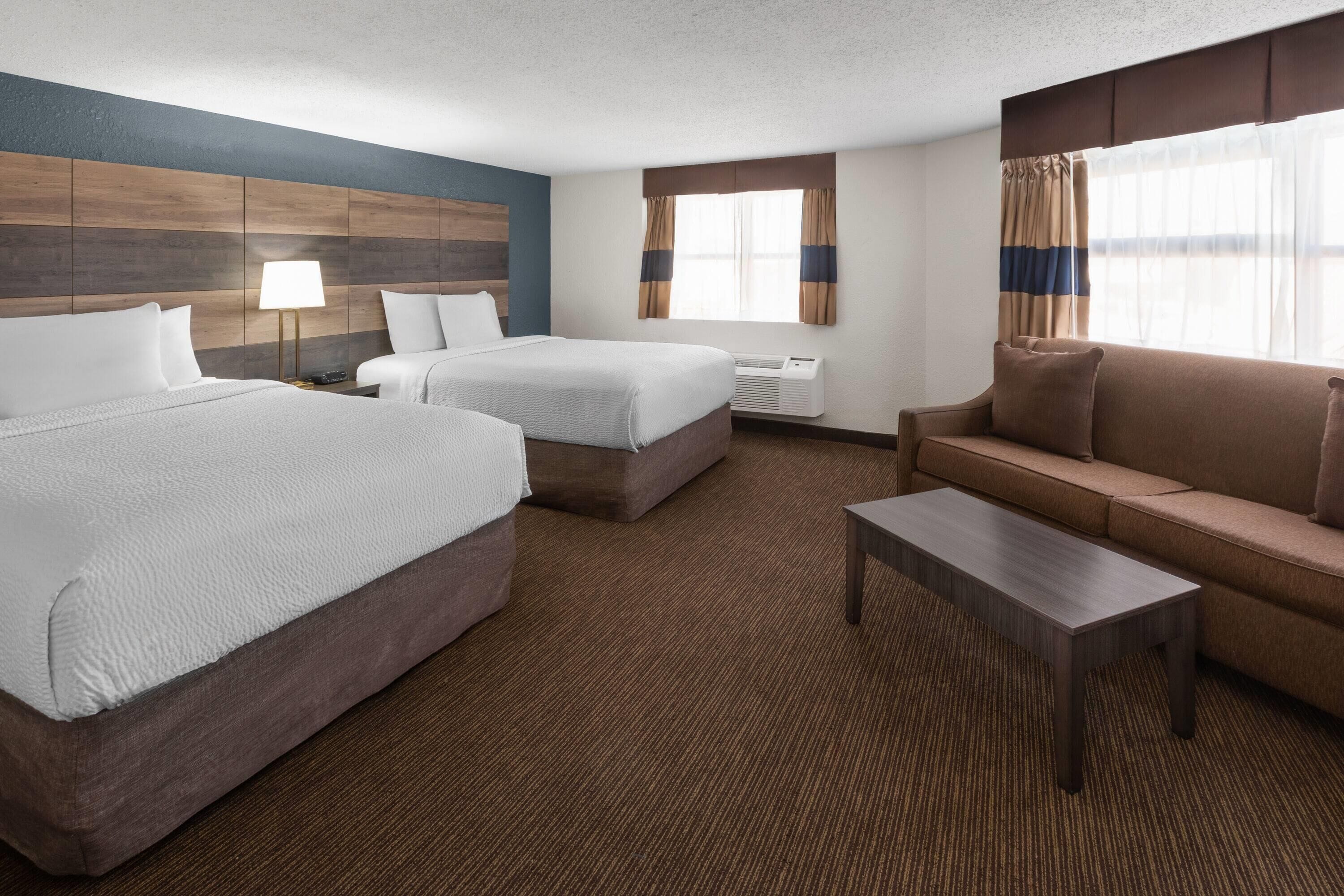 Habitación de hotel con dos camas, un sofá, una mesita de centro y una ventana con cortinas.