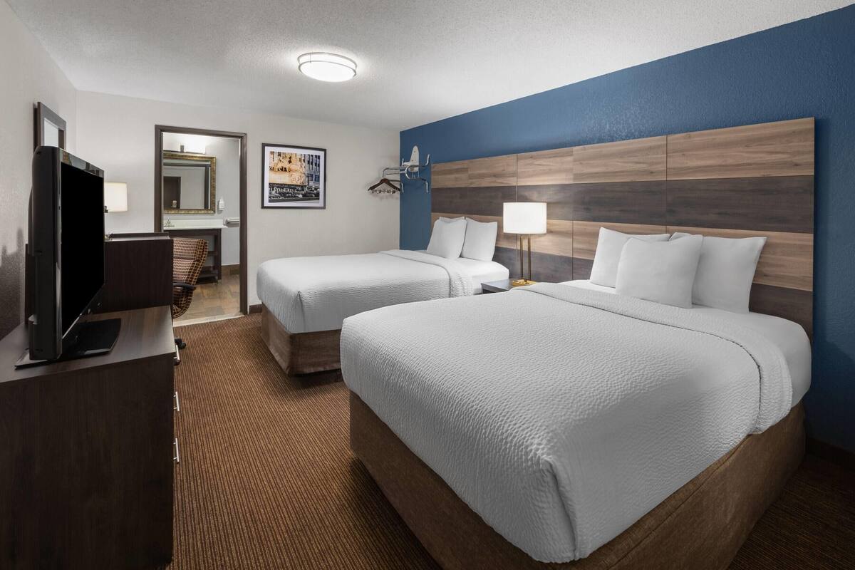 A hotel room with two beds, a TV, a desk, and a bathroom visible through an open door.