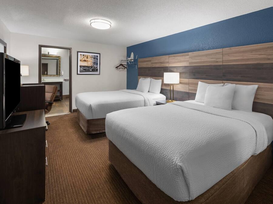 A hotel room with two beds, a TV, a desk, and a bathroom visible through an open door.