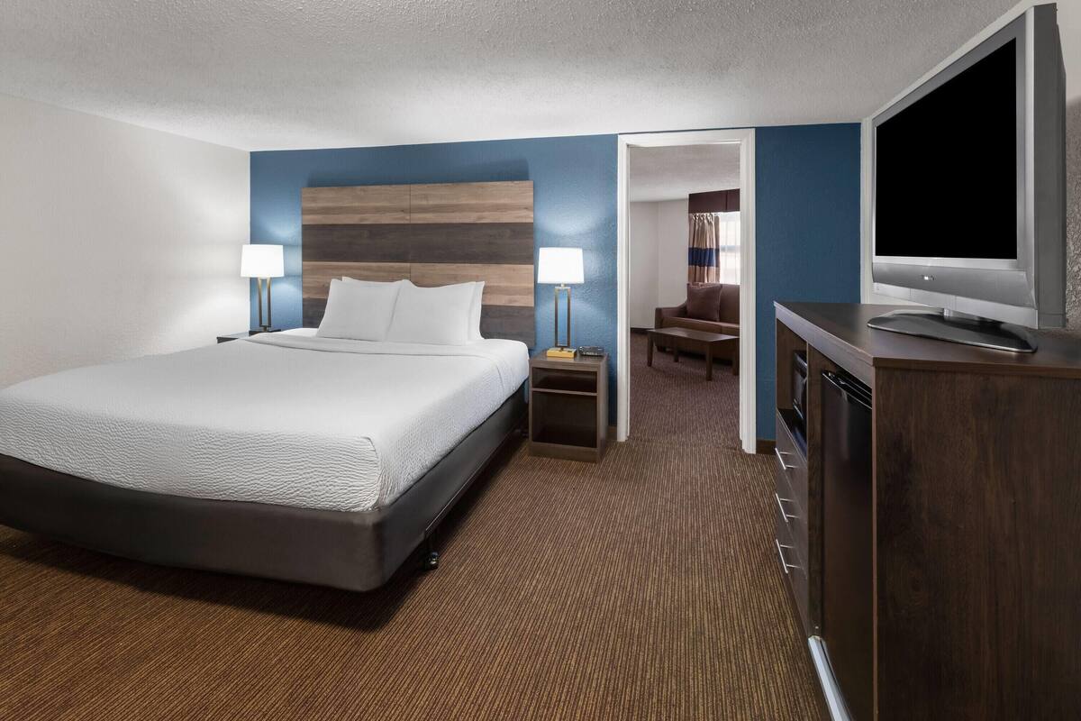 A hotel room with a large bed, bedside lamps, a flat-screen TV, and a wooden headboard.