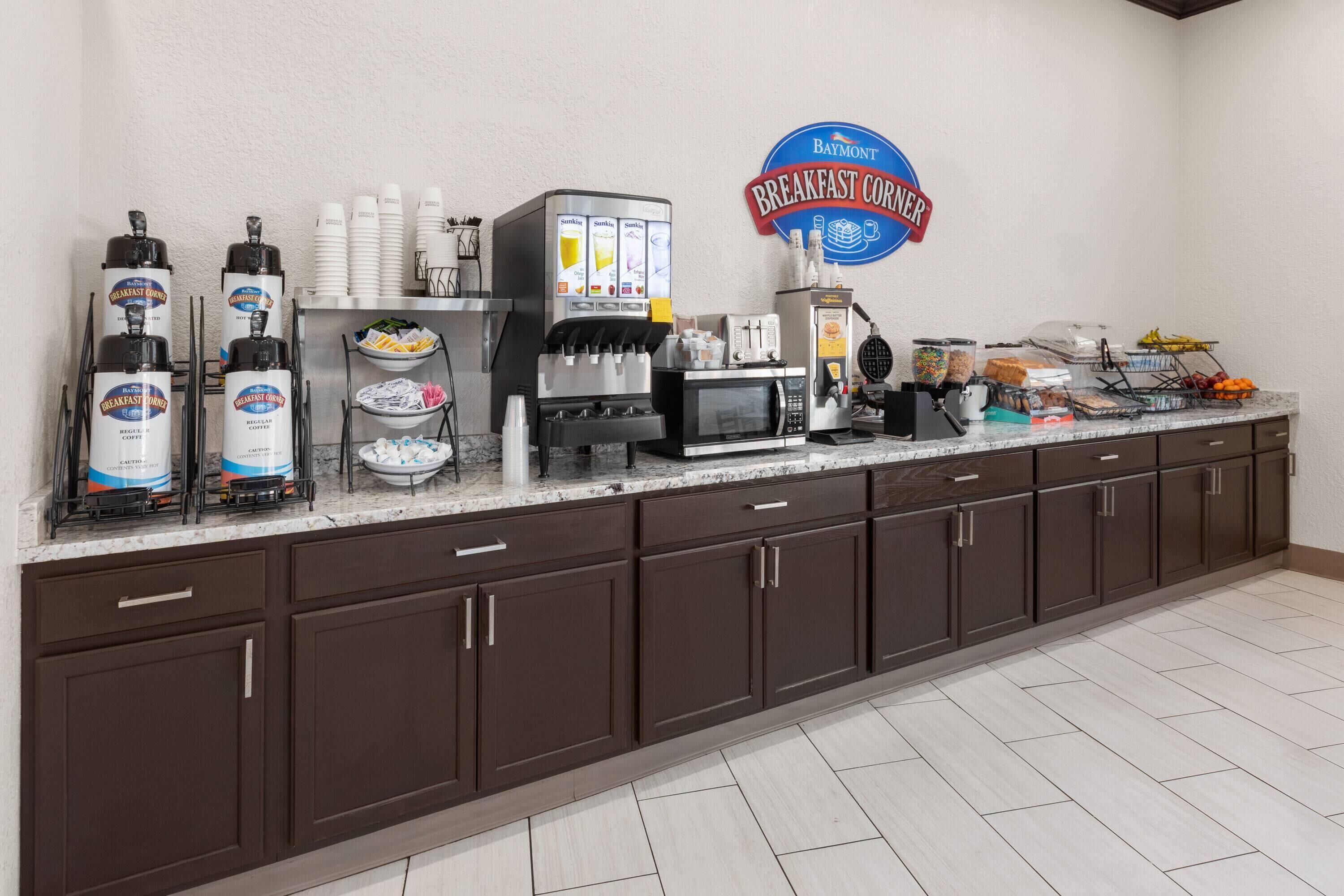 A breakfast counter with coffee dispensers, a microwave, and a sign for Baymont Breakfast Corner.