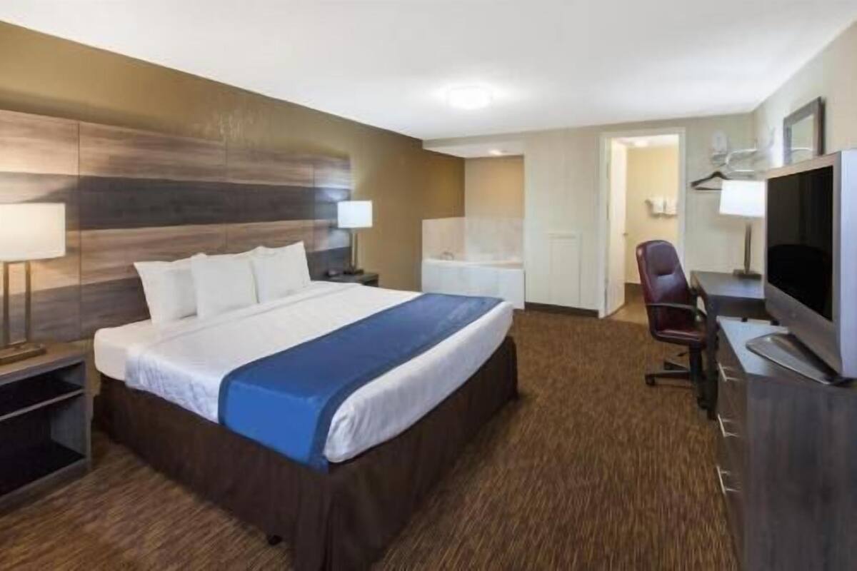A hotel room with a large bed, a desk with a chair, a television, and a bathroom visible through an open door.