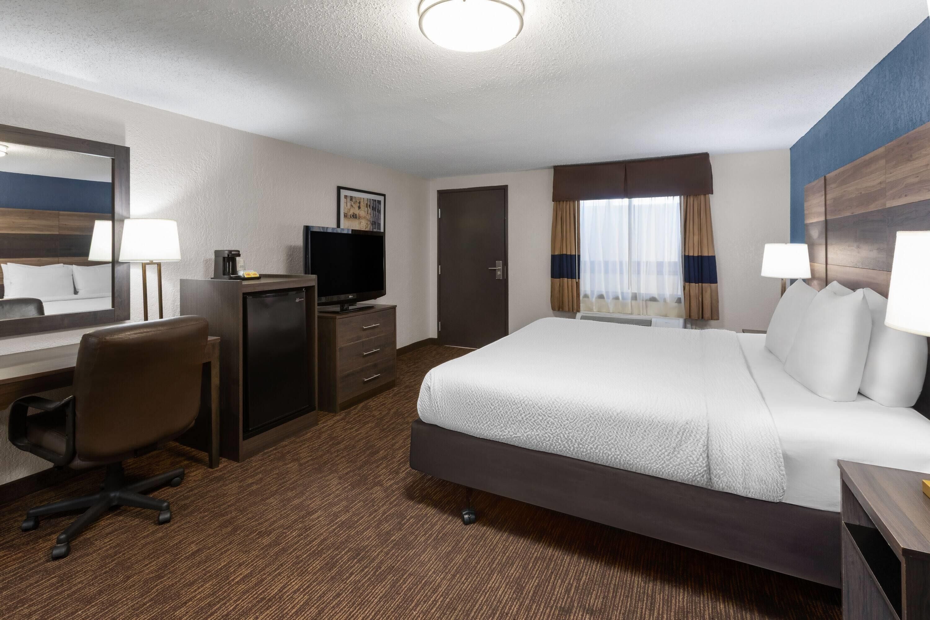 A hotel room with a large bed, a desk with a chair, a television, and a window with curtains.