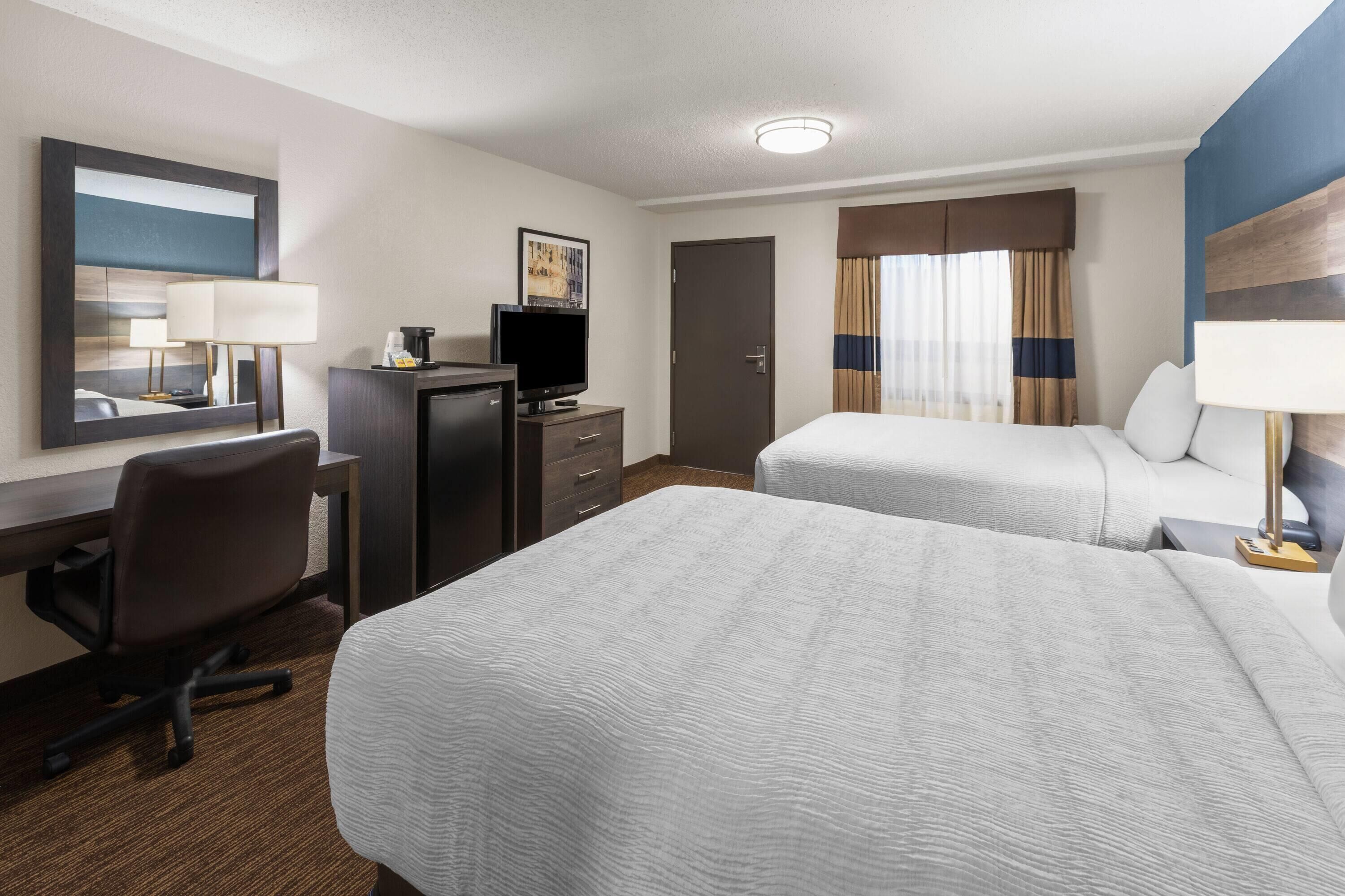 Quarto de hotel com duas camas, uma escrivaninha com cadeira, televisão e espelho.