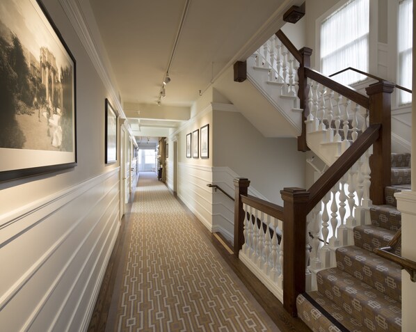 A hallway with a patterned carpet, a staircase with white balusters, and framed pictures on the walls.