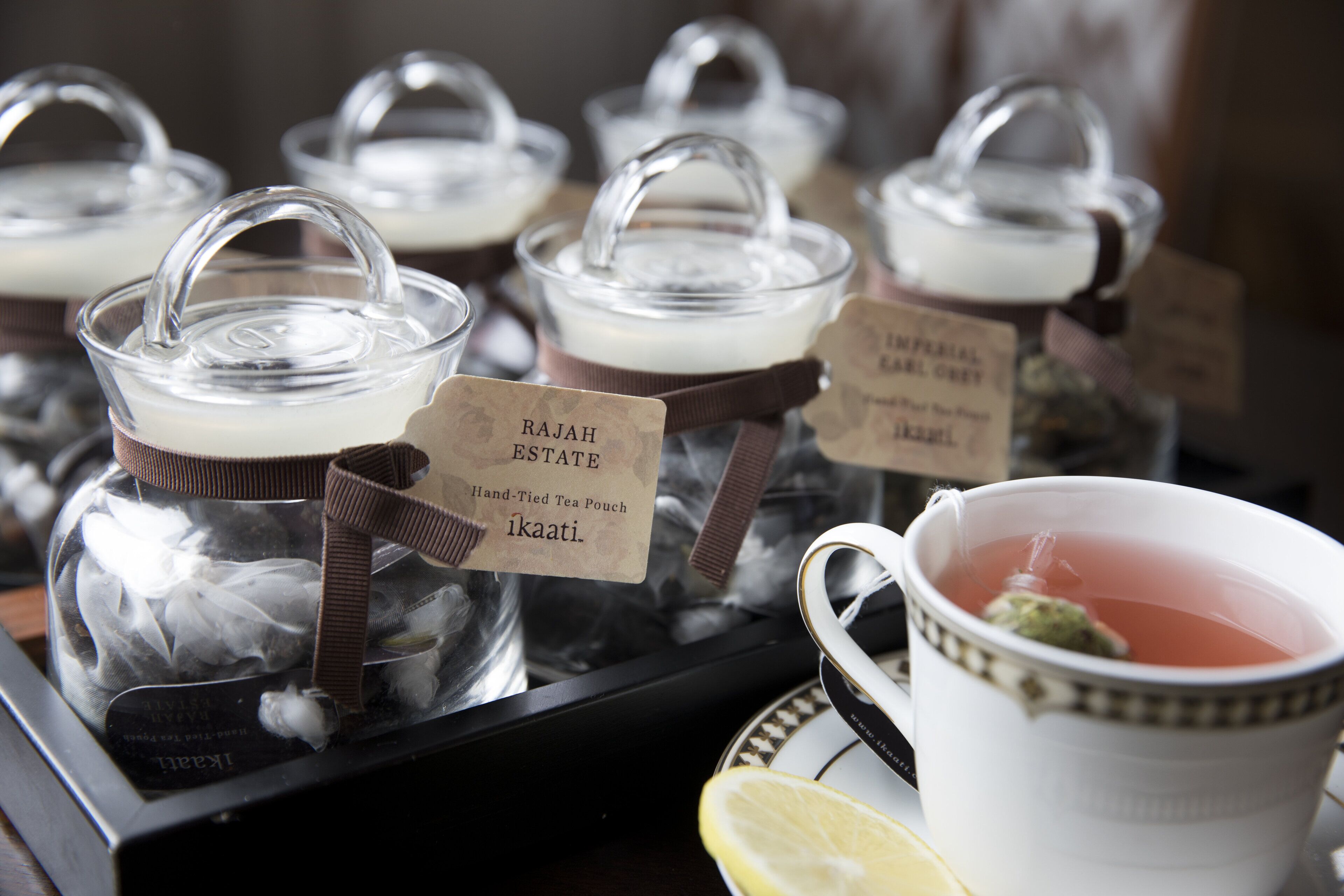 A tray with several glass containers labeled with tea names and a cup of tea with a lemon slice.