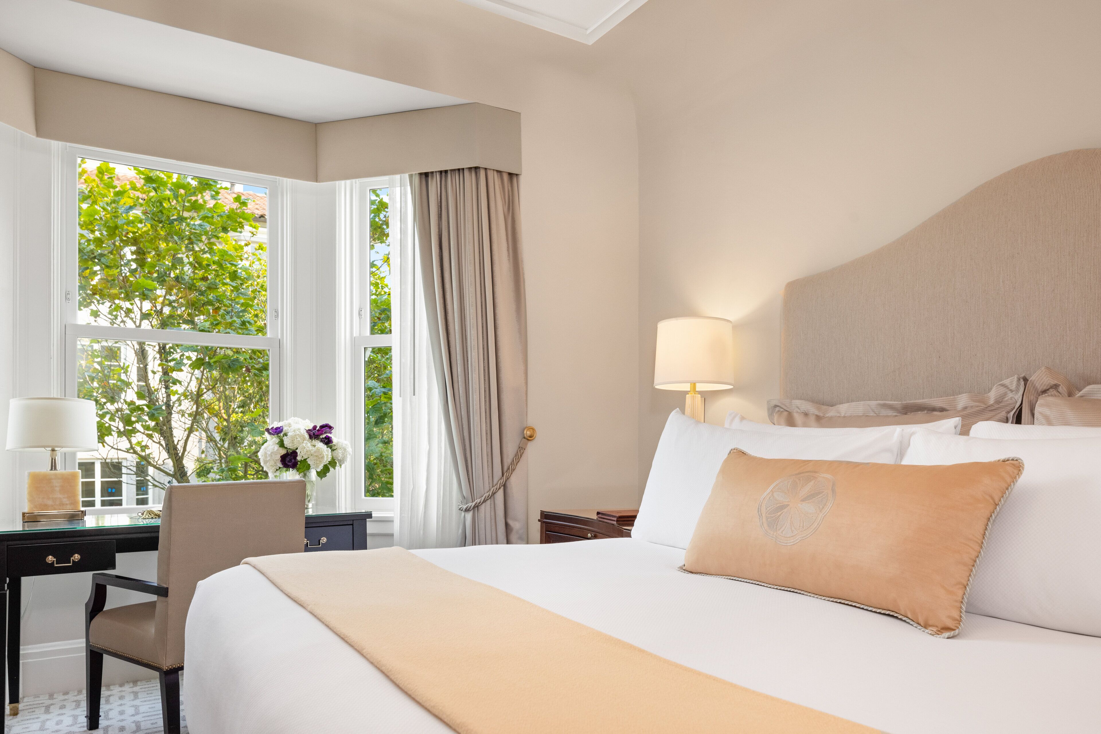 Une chambre d’hôtel avec un grand lit, un bureau avec une lampe, une chaise et une fenêtre avec des rideaux.