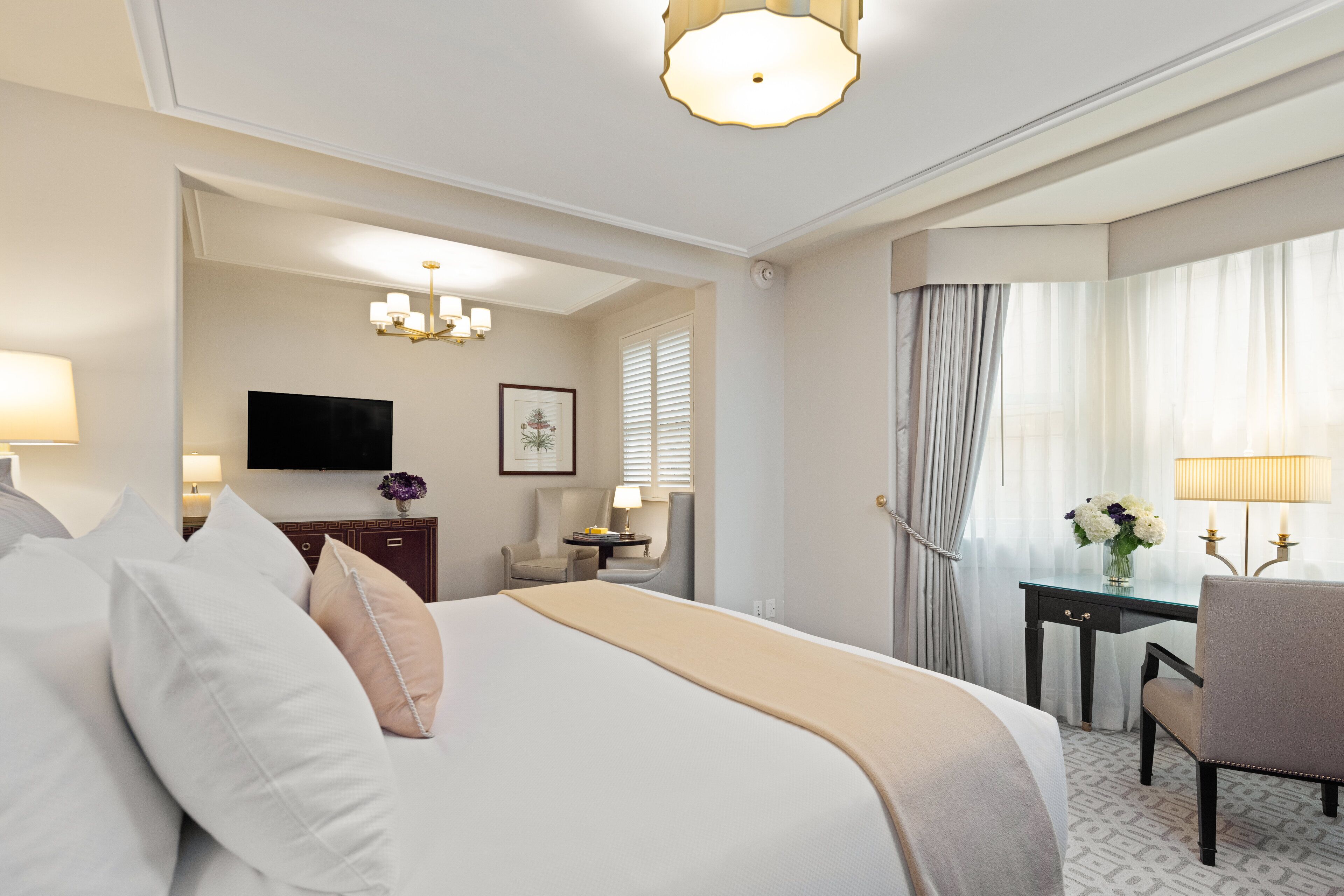 Una habitación de hotel con una cama grande, un escritorio con una silla, un televisor y una araña.