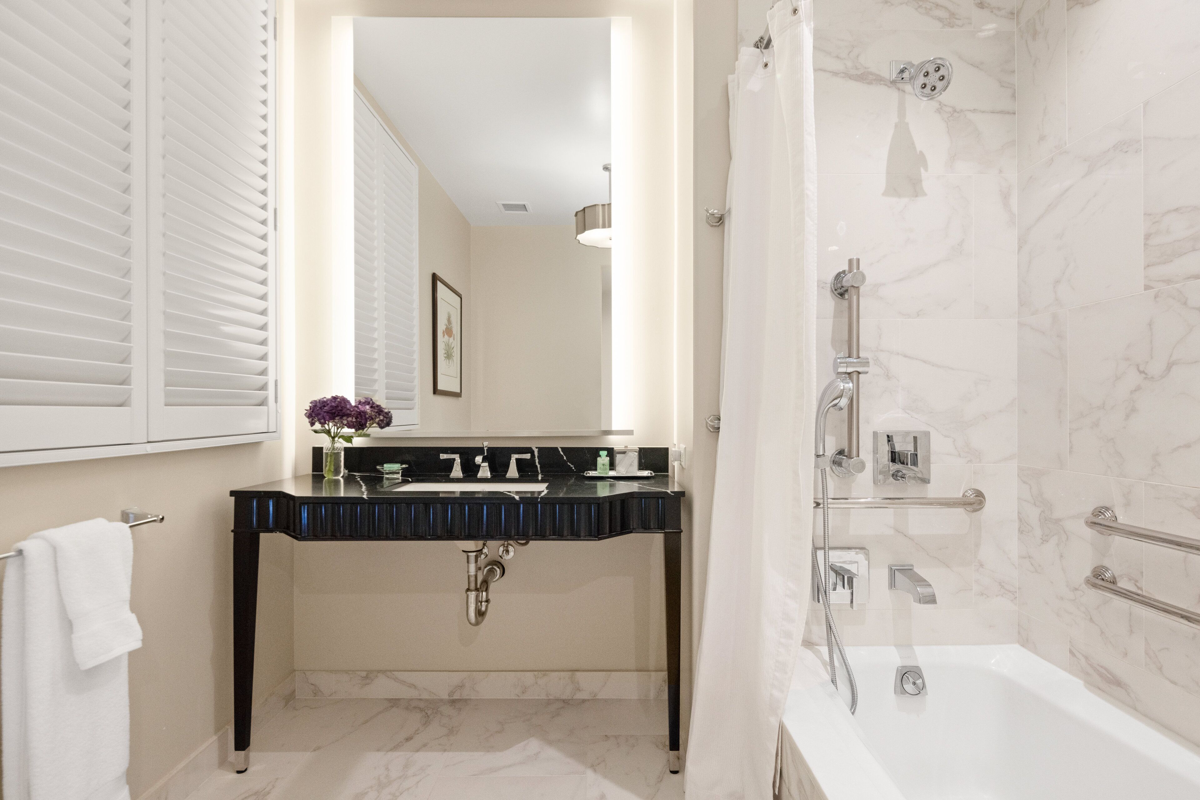 Un bagno moderno con un mobile lavabo nero, una vasca da bagno bianca e una parete doccia in marmo.