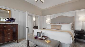 A hotel room with a bed, bedside tables, a dresser, a mirror, and a chandelier.