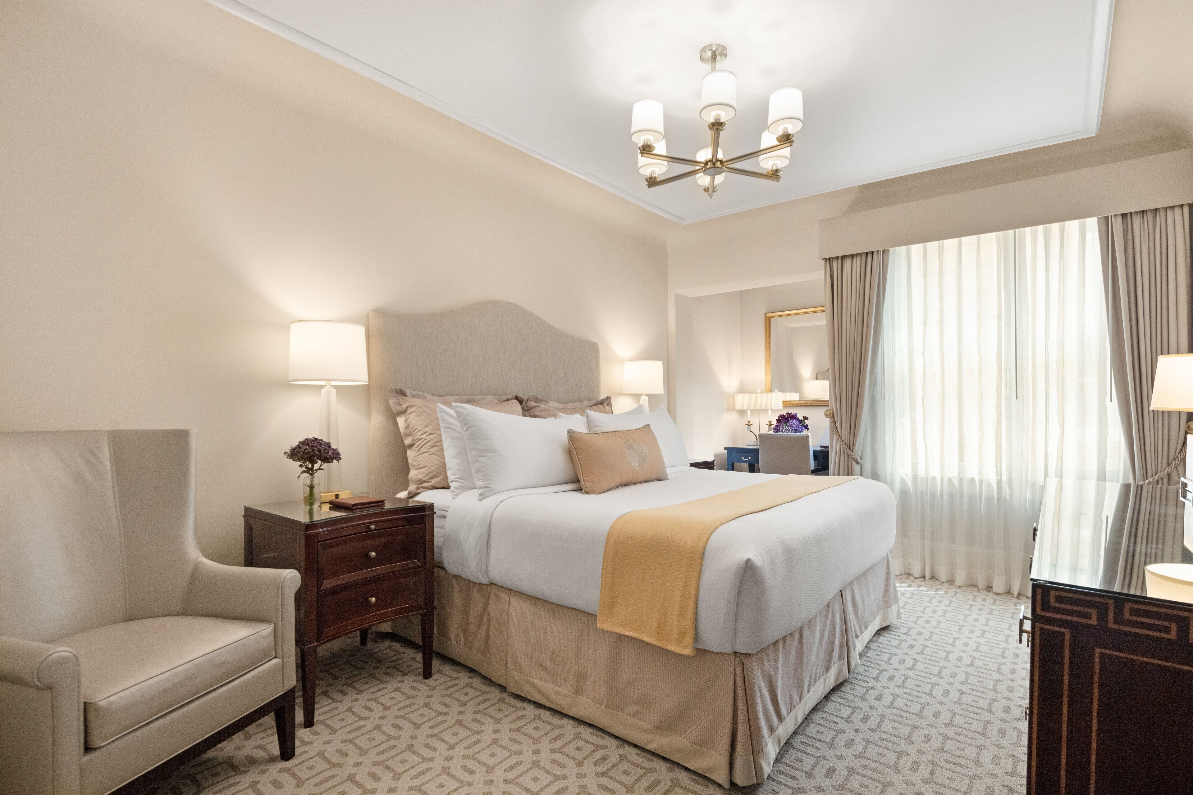 Camera d'albergo con un letto grande, lampade sui comodini, una sedia e un lampadario.