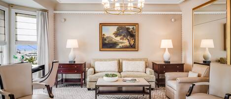 A well-lit living room with a sofa, armchairs, a coffee table, and a chandelier. There is a painting on the wall and a large mirror.