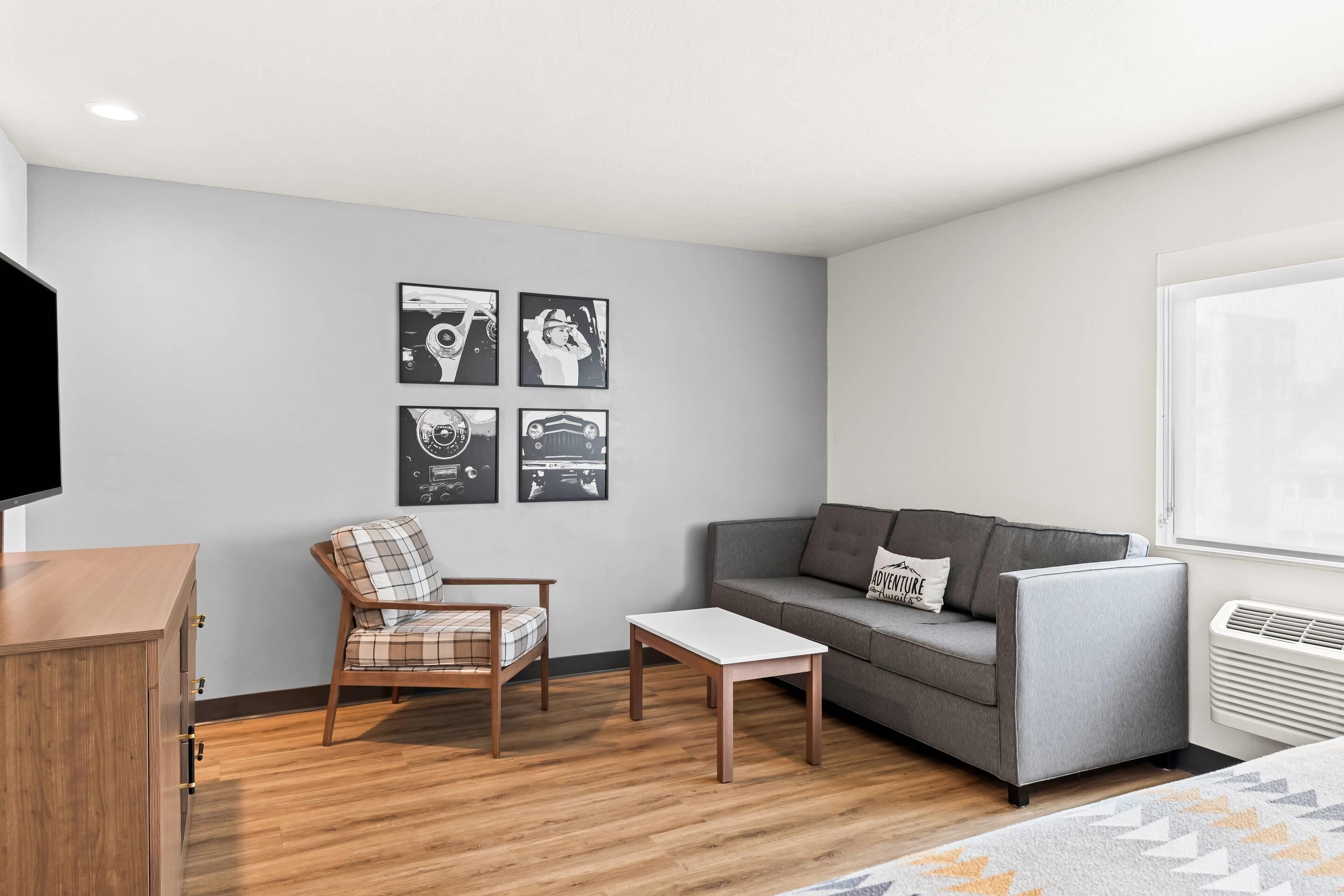 A modern living room with a sofa, armchair, and coffee table, a flat-screen TV, and four framed pictures on the wall.