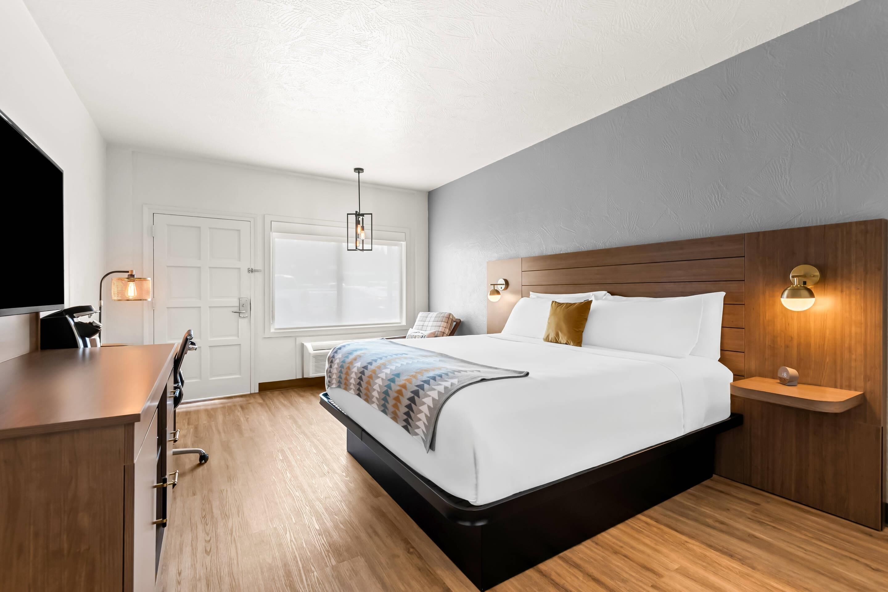 A modern hotel room with a large bed, a desk, and a window.