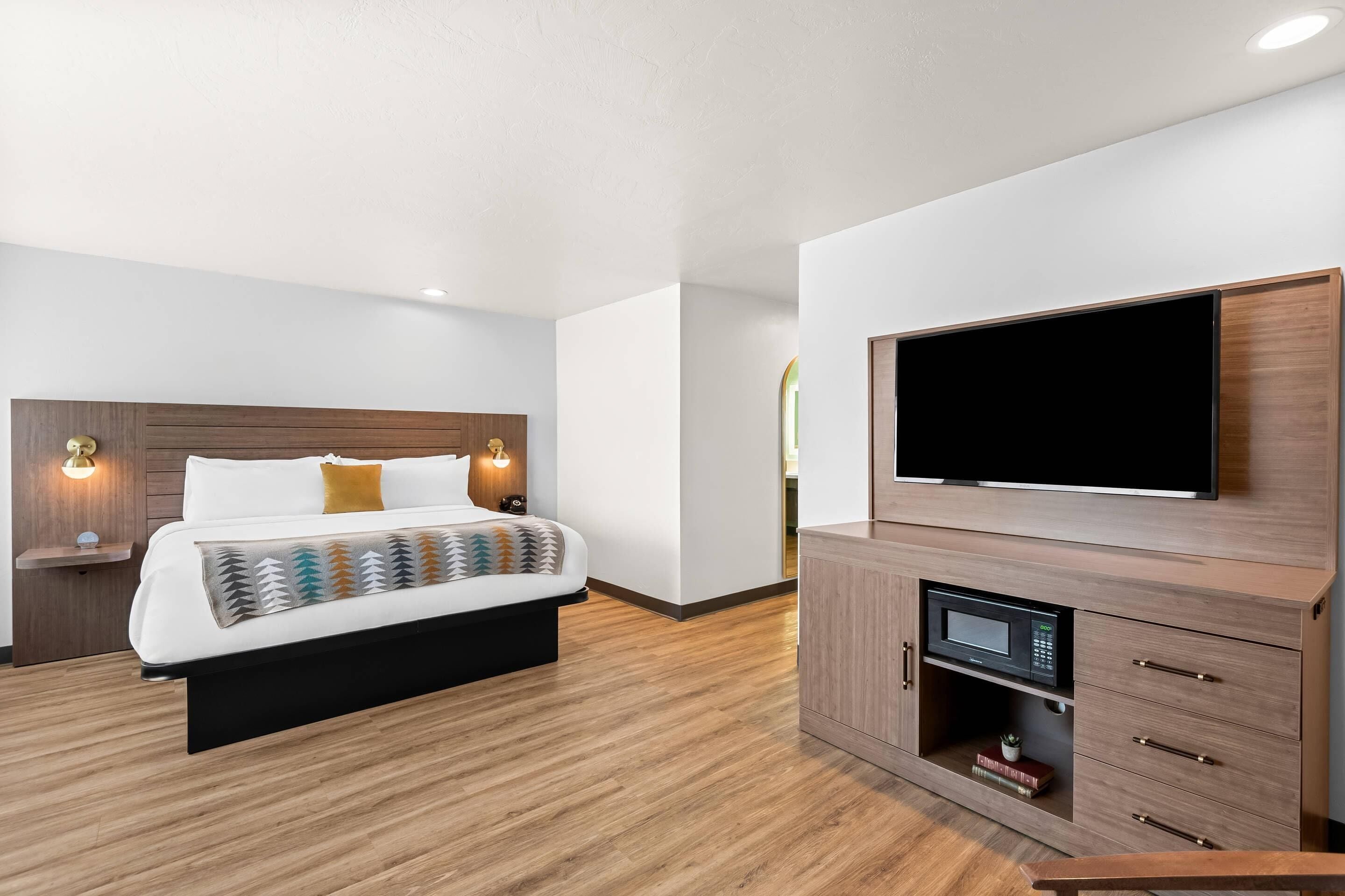 A modern hotel room with a large bed, a flat-screen TV, a built-in microwave, and a wooden cabinet.