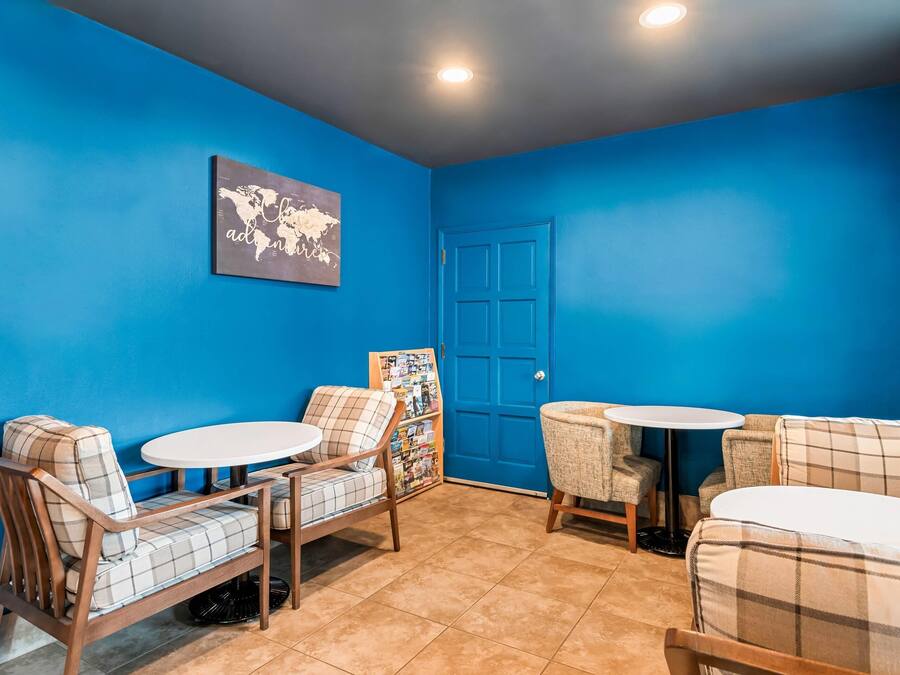 Una habitación con paredes azules, un cuadro de un mapa mundial, una puerta cerrada y una zona de estar con dos mesas redondas y sillas.