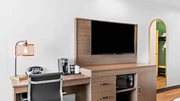 Ein Hotelzimmer mit Holztisch, Flachbildfernseher, Kaffeemaschine, Telefon und Spiegel.