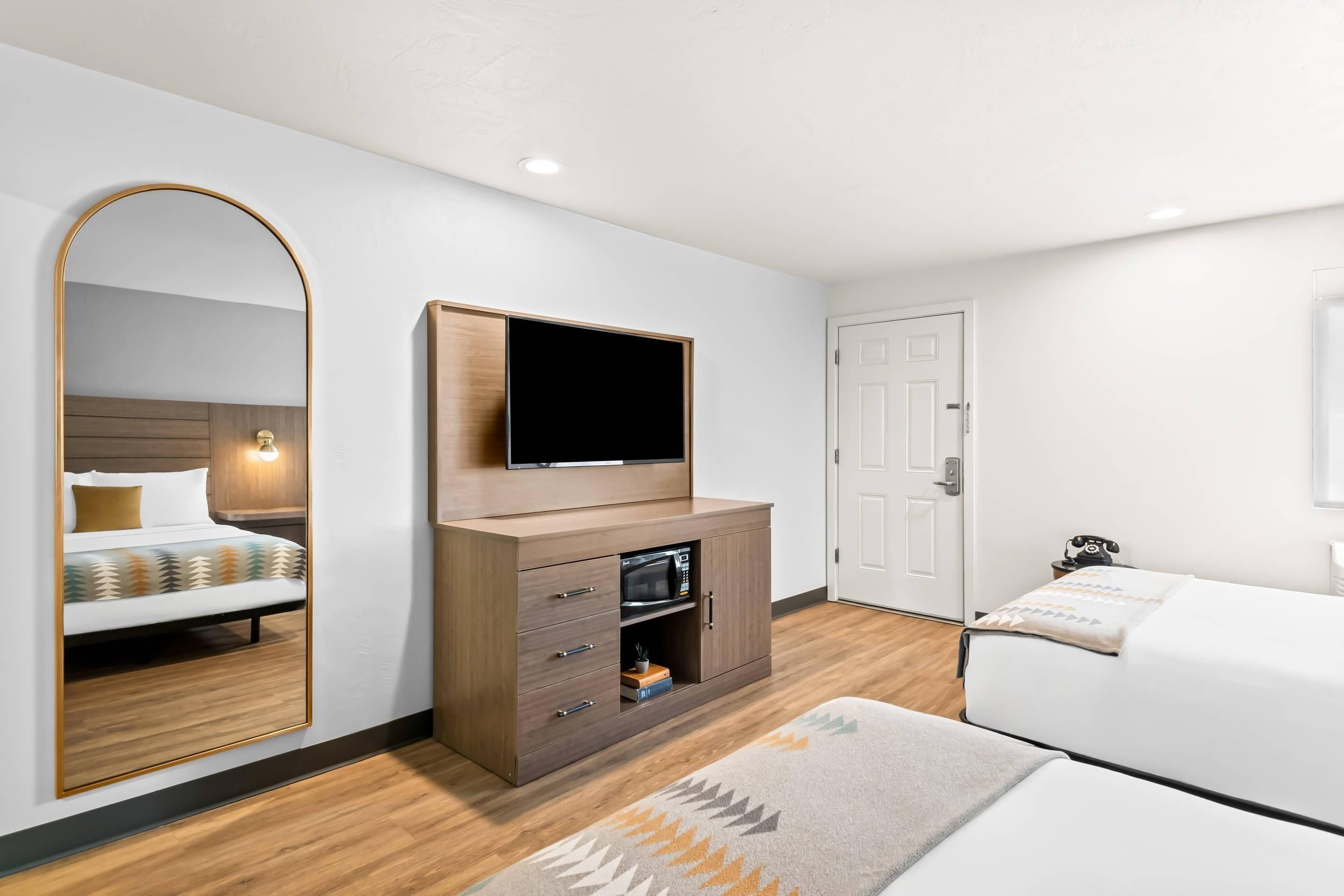 Une chambre d’hôtel avec un lit, un téléviseur fixé à un meuble en bois, un miroir et une porte.