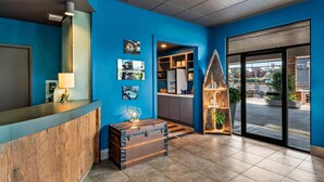 A reception area with a blue wall, a wooden reception desk, a trunk, and a view of the outside through large glass doors. - Maverick Hotel Eugene Near University, an Ascend Collection Hotel (Eugene)