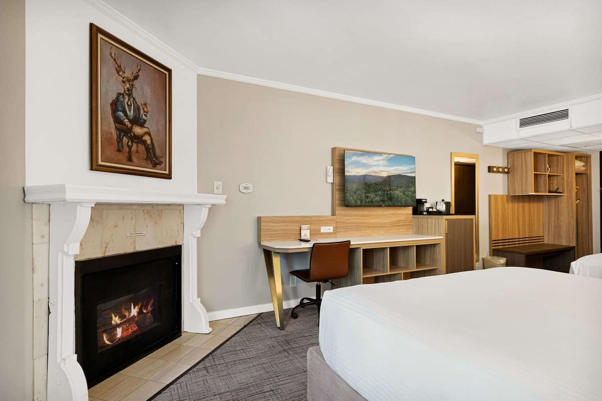 Une chambre d’hôtel avec une cheminée, un bureau, un lit et un tableau au mur.