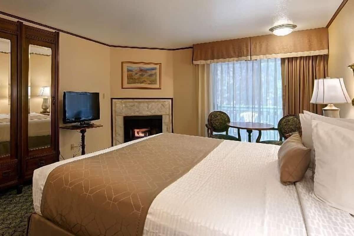Une chambre d’hôtel dotée d’un grand lit, d’une télévision, d’une cheminée, d’une table à manger avec des chaises et d’un balcon avec des rideaux.