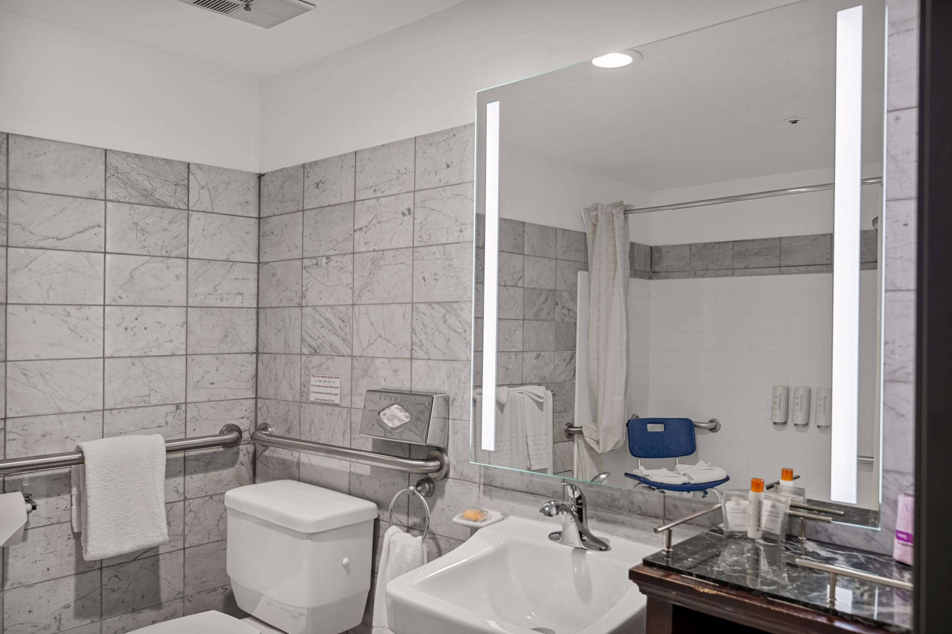 Un baño moderno con ducha de azulejos de mármol, inodoro blanco, lavabo con encimera de mármol y un espejo grande.