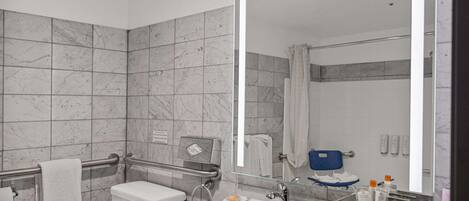 Un baño moderno con ducha de azulejos de mármol, inodoro blanco, lavabo con encimera de mármol y un espejo grande.