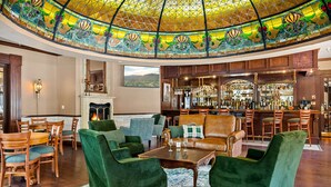 Eine großzügige Lobby mit Bar, grünen Polstersesseln und einer dekorativen Glasdecke.