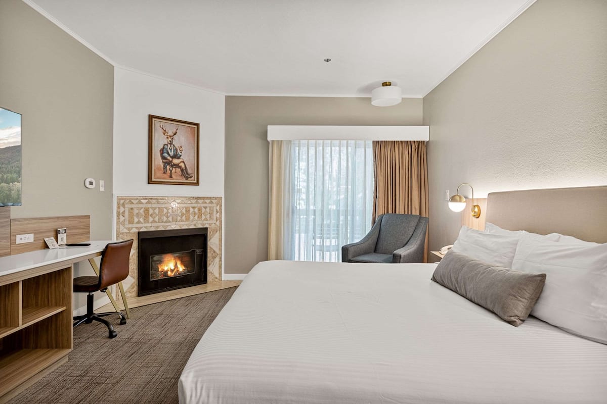 Une chambre d’hôtel avec un lit, un bureau, une chaise, une cheminée et une grande fenêtre avec des rideaux.