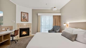 Habitación de hotel con cama, escritorio, silla, chimenea y un amplio ventanal con cortinas.