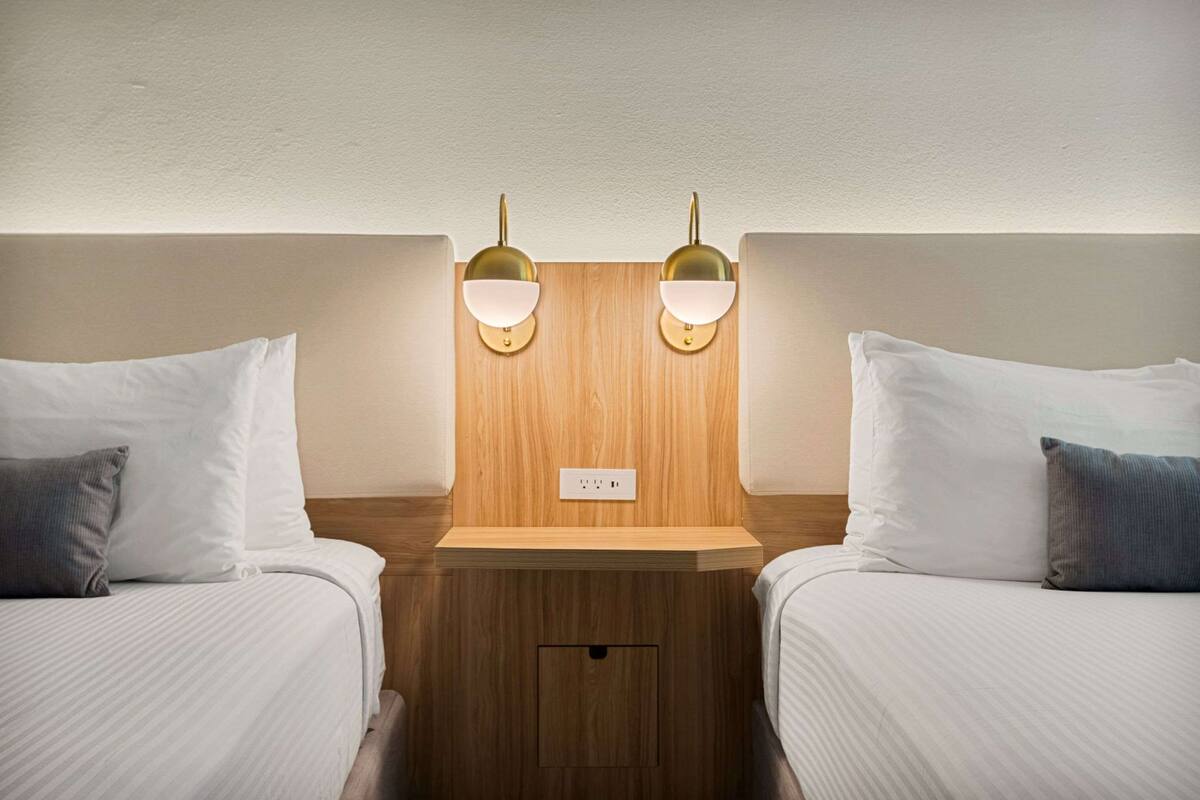 Une chambre d’hôtel avec deux lits, une tête de lit en bois et des appliques murales.