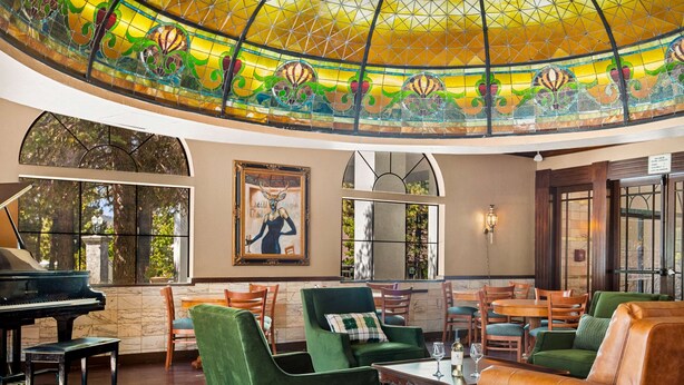 Ein geräumiger Lounge-Bereich mit einem Flügel, bequemen Sitzgelegenheiten und einer großen Decke aus farbigem Glas.