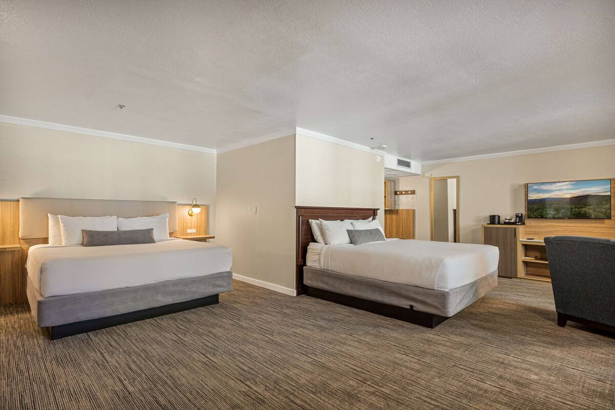 Une chambre d’hôtel avec deux lits, un bureau, une chaise et un tableau au mur.