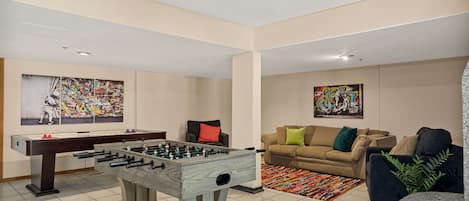 A living room with a foosball table, a sofa, and two paintings on the walls.