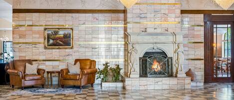 Un vestíbulo con piso a cuadros, chimenea, sillones de cuero y candelabro.