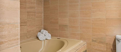A bathroom with beige tiles, a bathtub, and a toilet.