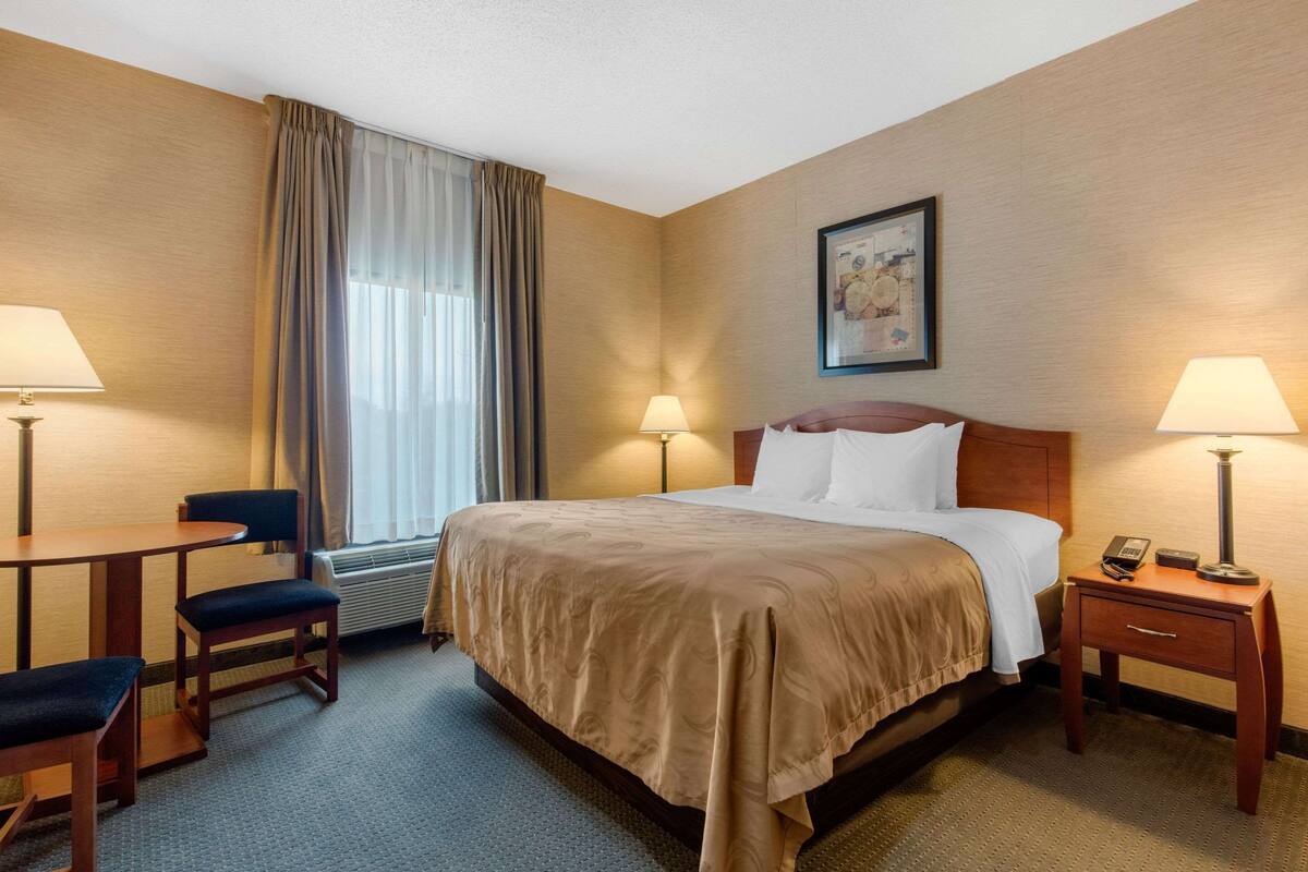A hotel room with a bed, two bedside tables with lamps, a chair, and a window with curtains.