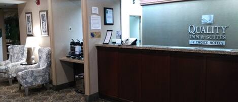 A hotel reception area with a reception desk, framed pictures on the wall, and a carpeted floor.