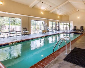 An indoor swimming pool with clear water, surrounded by lounge chairs and a sunlit patio area. - Quality Inn & Suites Benton - Draffenville (Benton)