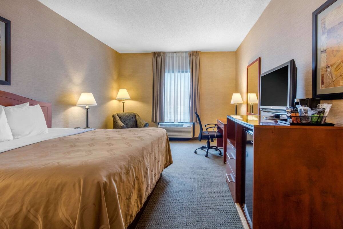 A hotel room with a bed, desk, chair, TV, and a large window with curtains.