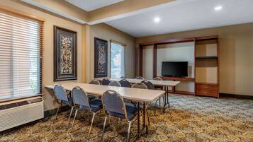 A conference room with a carpeted floor, a large TV screen, and framed artwork on the walls.