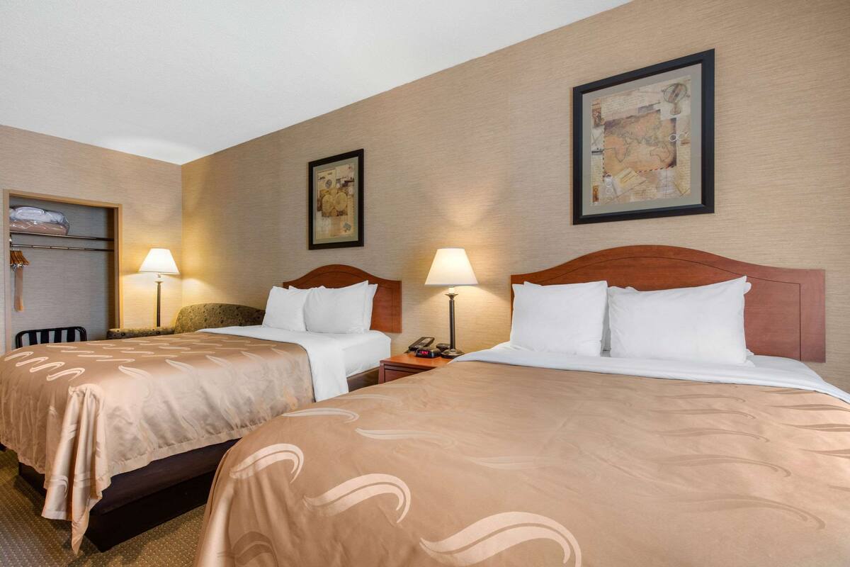 A hotel room with two beds, each with a wooden headboard, a nightstand with a lamp, and a framed map on the wall.